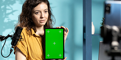 Woman with dark hair holding a tablet with a green screen in a studio setting.