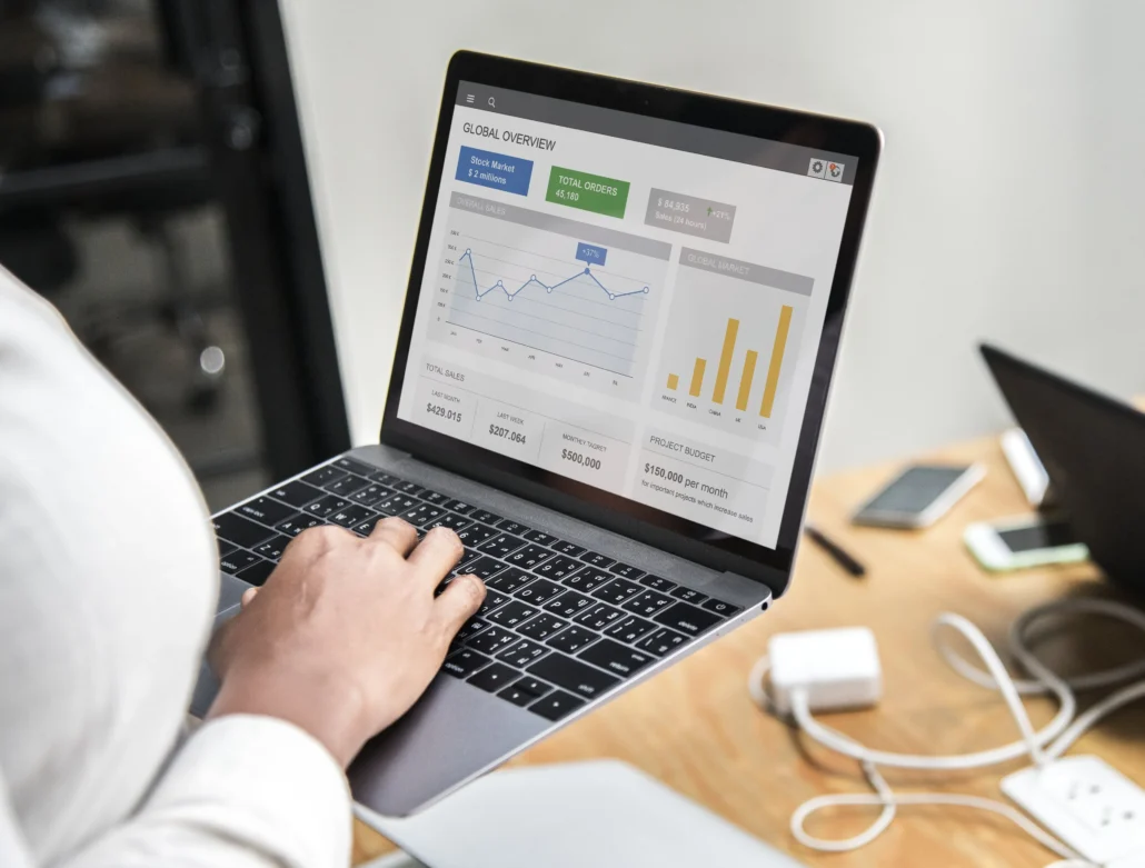 Person using a laptop to display a global overview dashboard with graphs and data metrics.